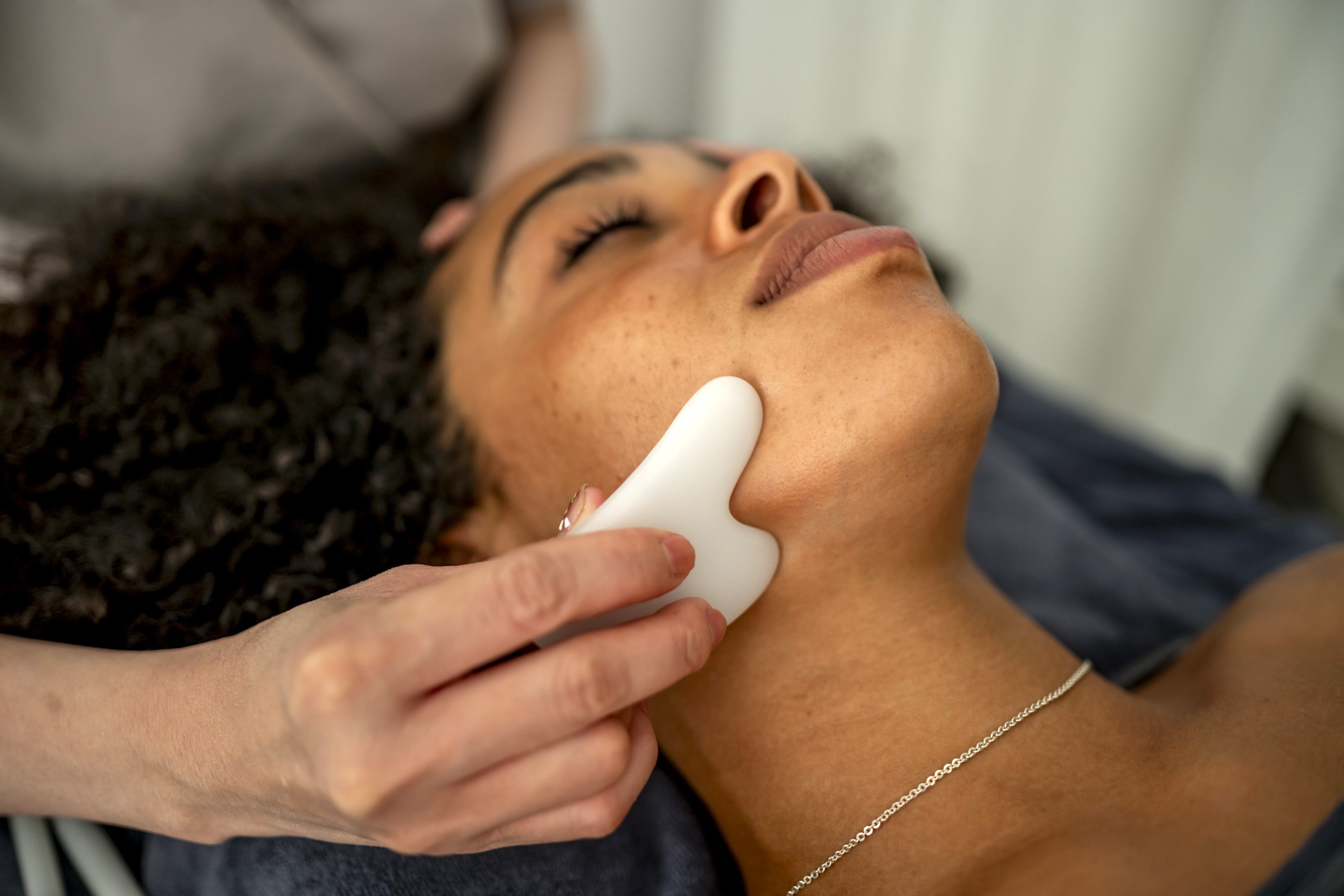 A serene moment of a woman enjoying a relaxing gua sha facial massage at a spa. The practitioner uses a smooth tool on her face, promoting wellness and relaxation.